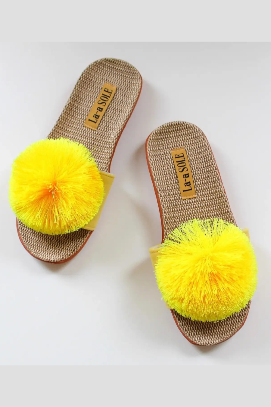 La-a SOLE Pom Pom Slides in vibrant colors, featuring soft fabric straps with playful pom pom embellishments.