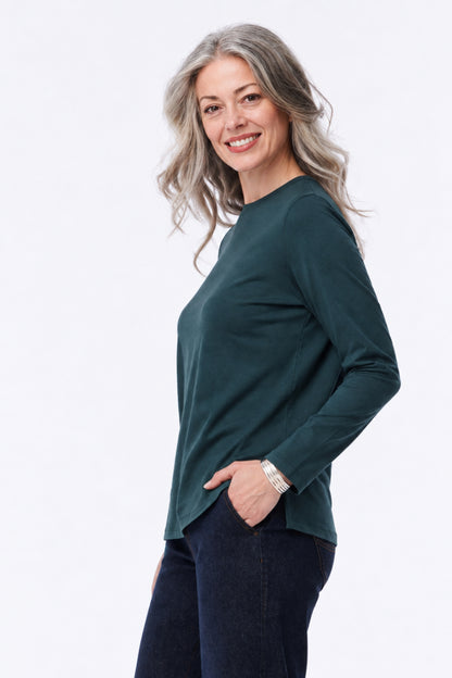 A smiling woman with gray hair is shown in profile wearing a dark green long-sleeve top and dark blue jeans against a plain white studio background.