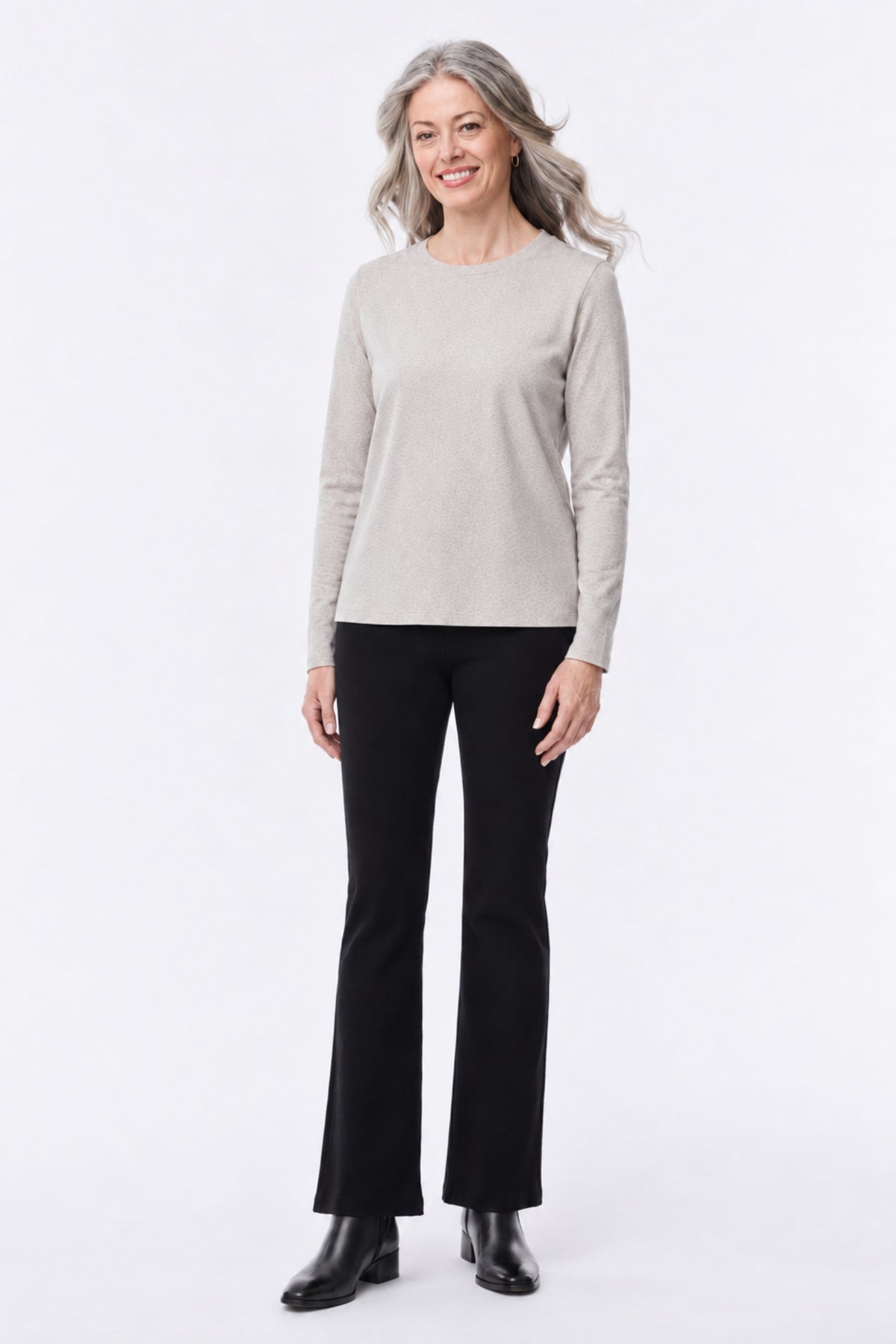 A woman modeling a light beige long-sleeve crewneck sweater and black flared pants against a plain white studio background.