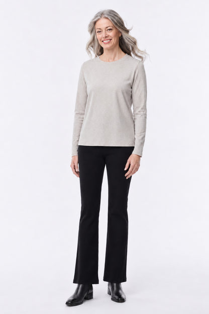 A woman modeling a light beige long-sleeve crewneck sweater and black flared pants against a plain white studio background.