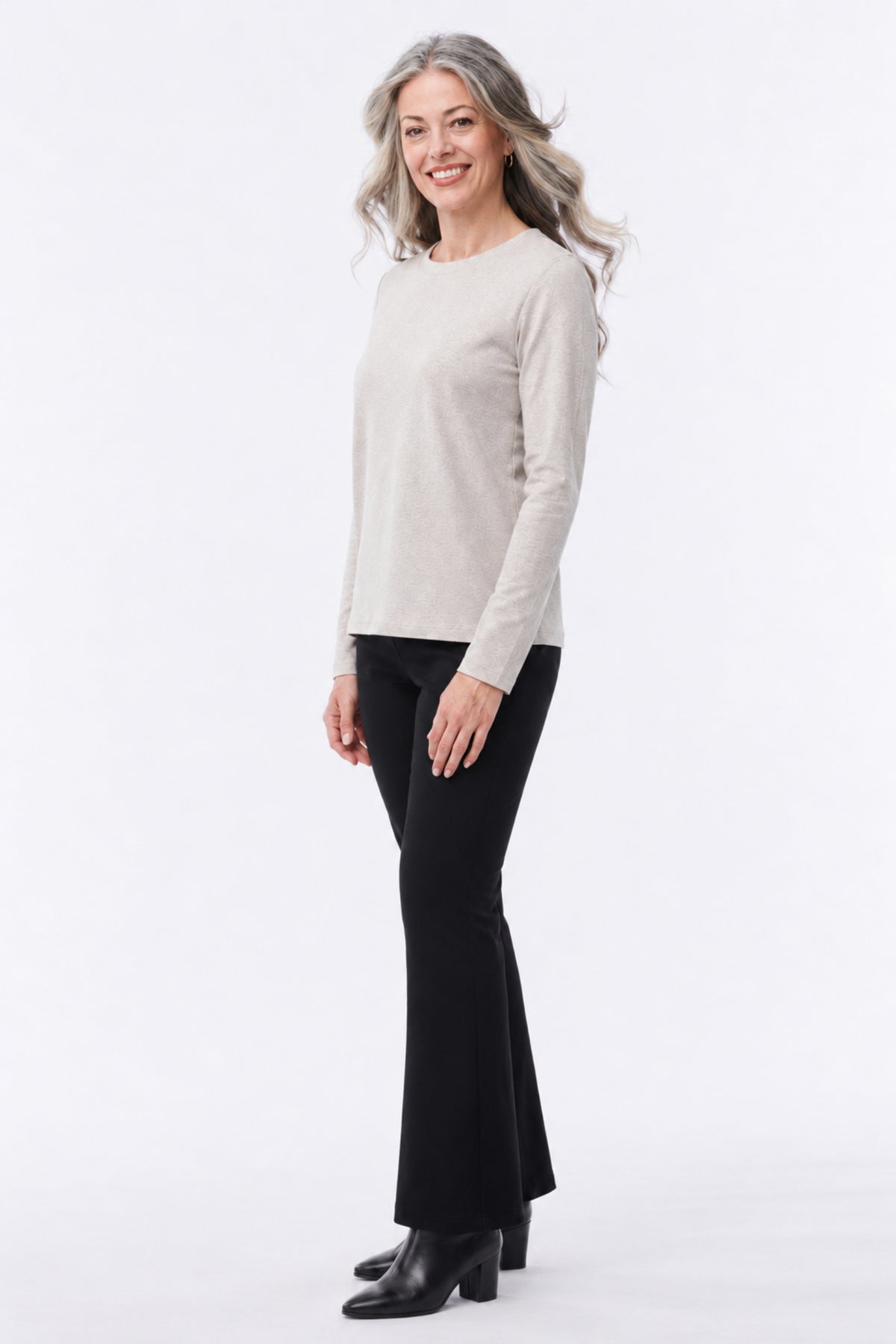 A woman modeling a light beige long-sleeve knit top and black flared pants against a plain white studio background.