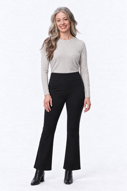 A woman modeling black high-waisted flared pants with a light gray long-sleeve top, standing against a plain white studio background.