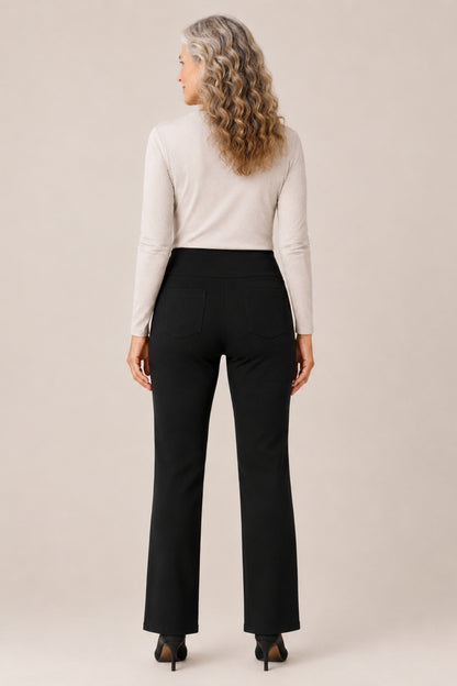 A woman with long, wavy blonde hair is shown from the back wearing a cream mock-neck long-sleeve top and black high-waisted flared pants, paired with black heels, against a solid light beige studio background.