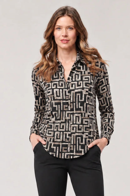 A woman modeling a long-sleeve button-up blouse with a black and beige geometric maze-like pattern, paired with black pants, against a light gray studio background.