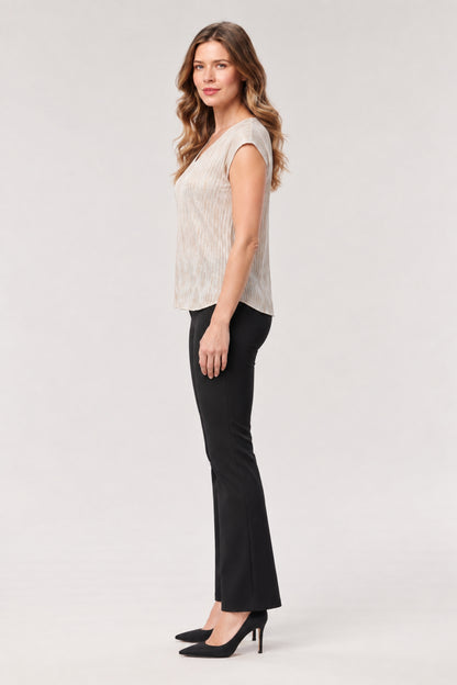 A woman modeling a sleeveless textured top in a light beige/cream color paired with black flared pants and black heels, standing against a plain light gray studio background.