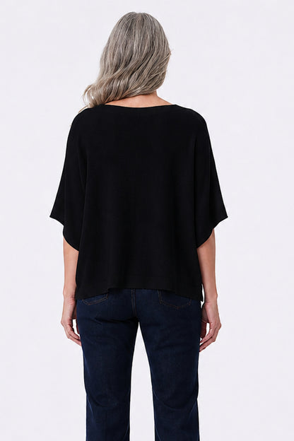 A woman viewed from the back wearing a loose black short-sleeve top and dark blue jeans against a plain light gray studio background.