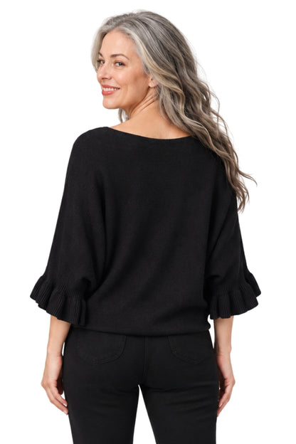 A woman with gray hair is shown from the back wearing a black boat-neck knit top with ruffled three-quarter sleeves and black pants, against a plain white background.