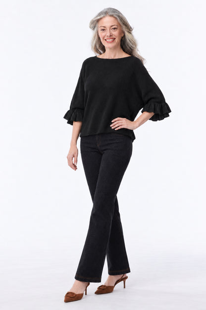 A woman modeling a black off-the-shoulder blouse with ruffled three-quarter sleeves and black flared pants, paired with brown pointed-toe heels, against a plain white studio background.