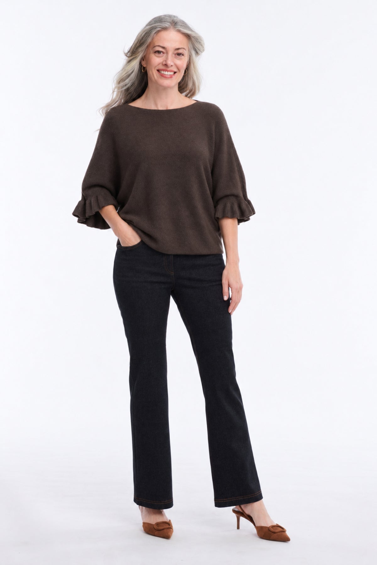 A woman modeling a dark brown boat-neck top with ruffled elbow-length sleeves, paired with black pants and brown heels, against a plain white studio background.