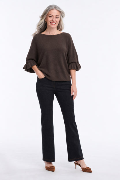 A woman modeling a dark brown boat-neck top with ruffled elbow-length sleeves, paired with black pants and brown heels, against a plain white studio background.