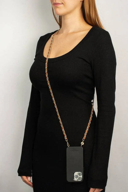 A woman wearing a black long-sleeve top and black dress, wearing a gold chain crossbody bag with a black pouch over her shoulder, against a light gray background.