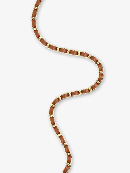 A close-up of a gold chain necklace with alternating brown and gold links, arranged in a S-shape on a light gray background.