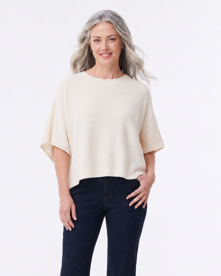 A woman modeling a cream short-sleeve knit top and dark navy wide-leg jeans with brown pointed-toe heels, photographed against a clean white studio background.
