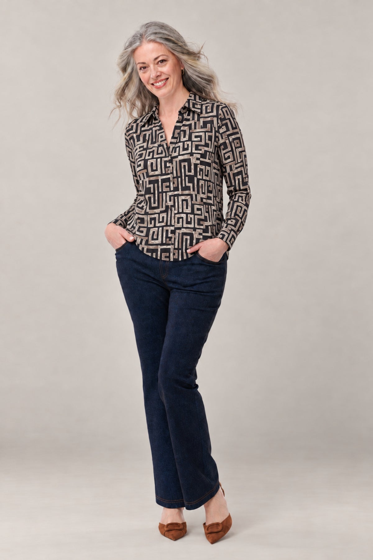 A woman modeling a long-sleeve button-up shirt with a black and beige geometric maze pattern, paired with dark blue jeans and brown shoes, against a neutral studio background.