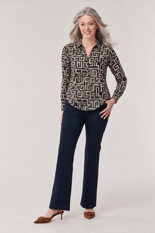 A woman modeling a long-sleeve button-up blouse with a black and beige geometric maze pattern, paired with dark blue jeans and brown pointed-toe heels, against a light gray studio background.