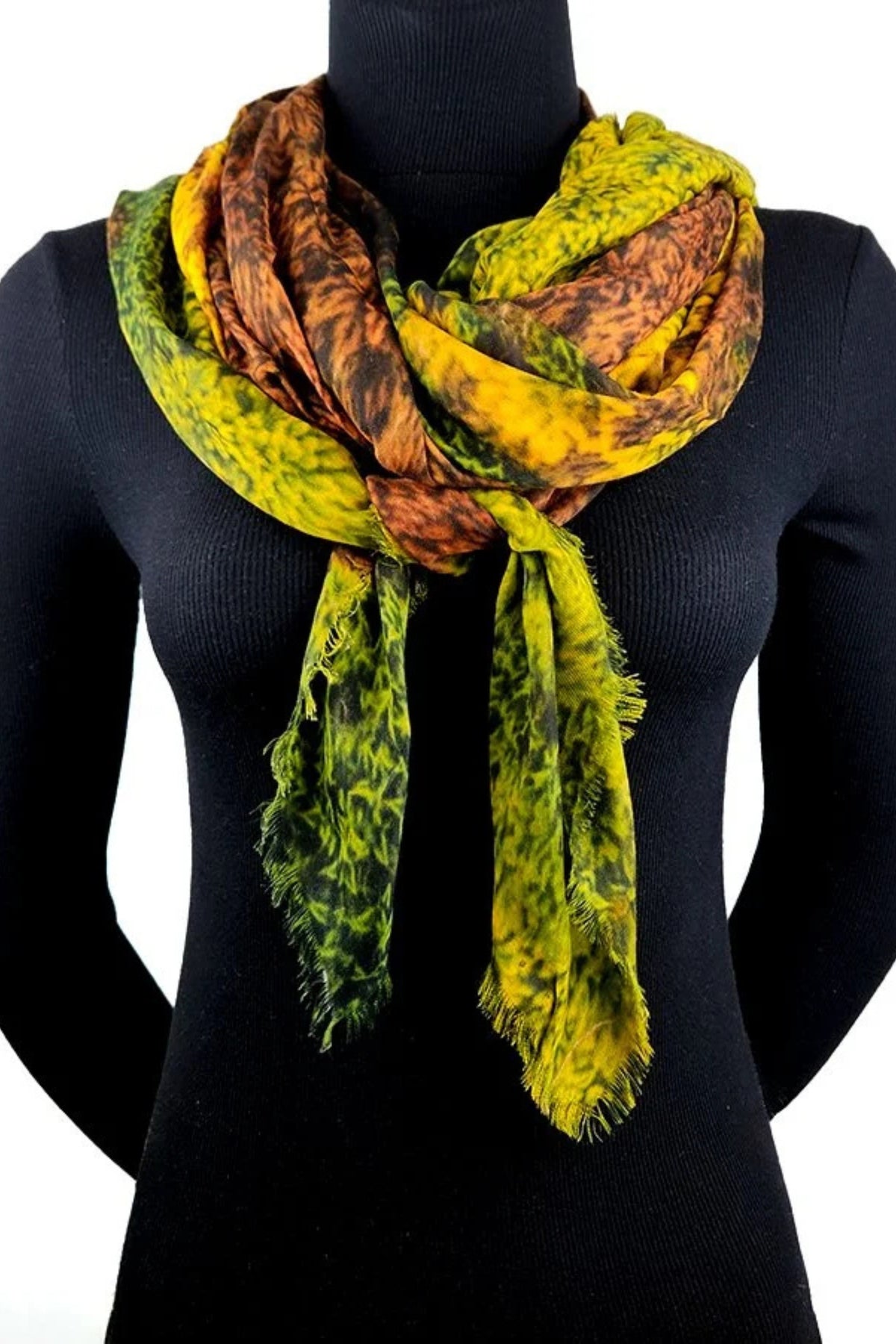 A multicolor scarf with yellow, green, and brown abstract patterns, draped on a black mannequin torso against a white background.