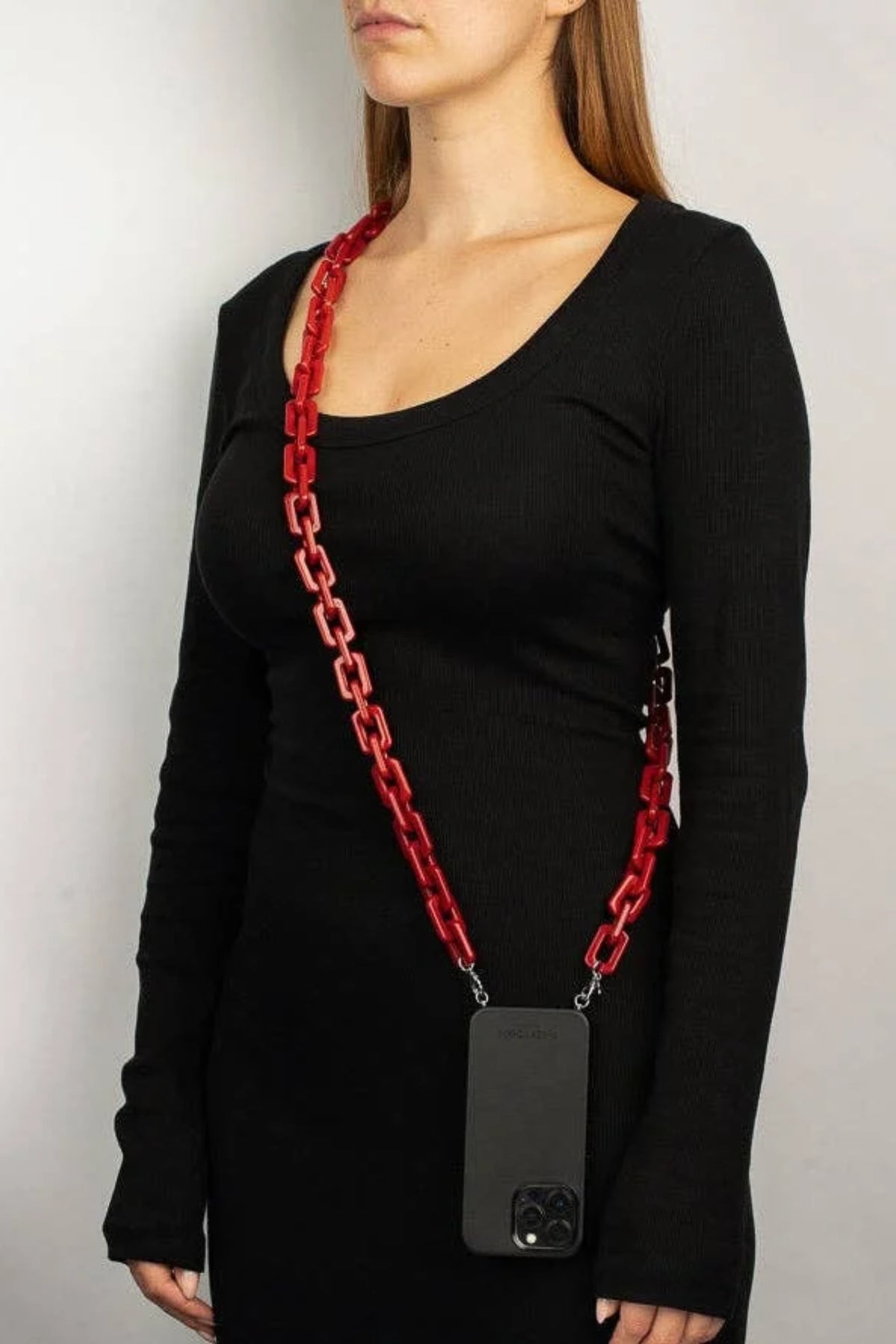 A woman wearing a black long-sleeve top models a red chunky chain phone strap holding a black smartphone case against a plain light gray background.