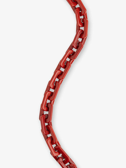 A close-up of a glossy red chain necklace or strap curving vertically against a plain light gray background.